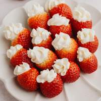 Several cheesecake stuffed strawberries on a white scalloped plate.