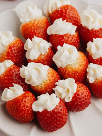 Several cheesecake stuffed strawberries on a white scalloped plate.