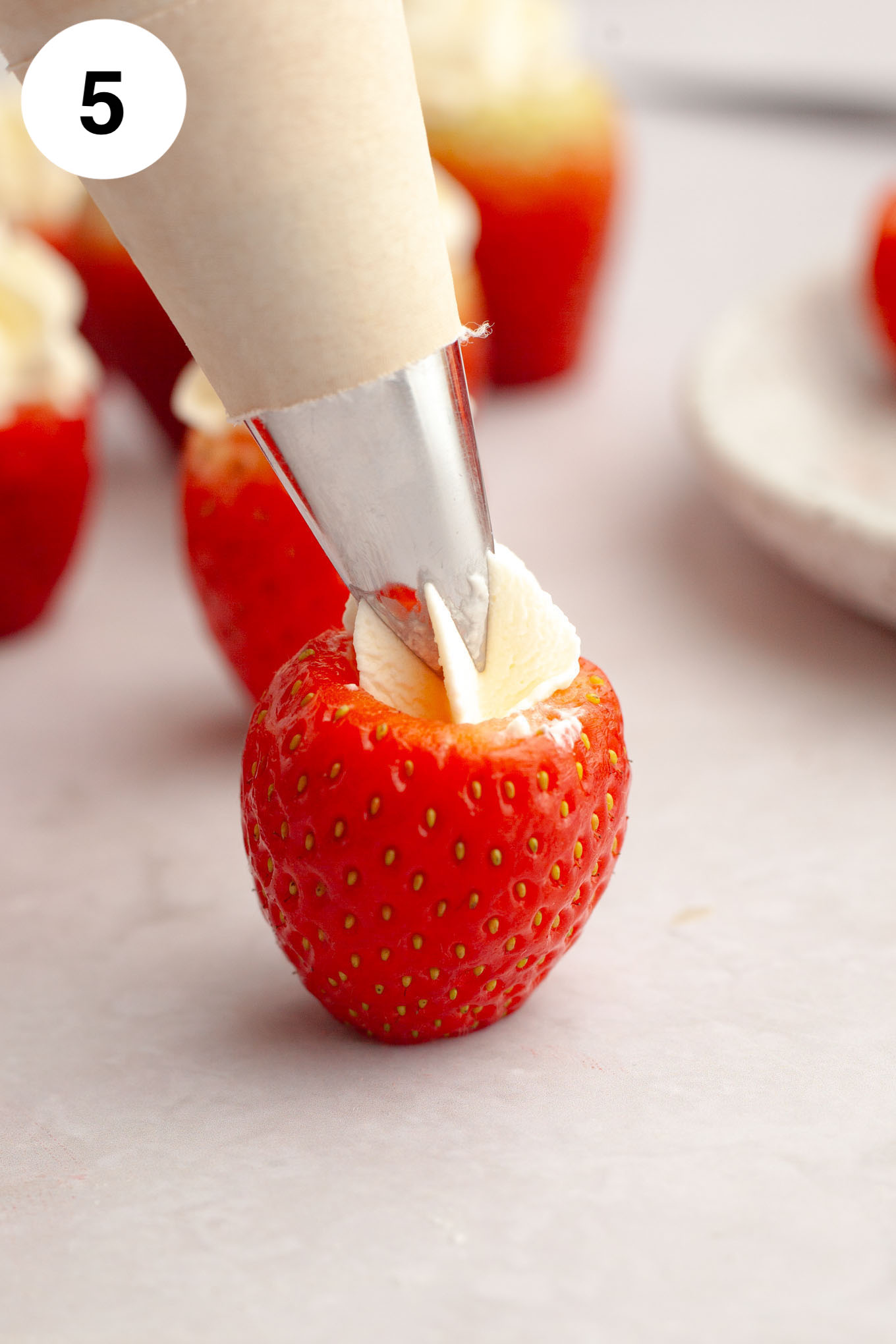 A process shot showing a fresh strawberry being filled with cheesecake filling. 