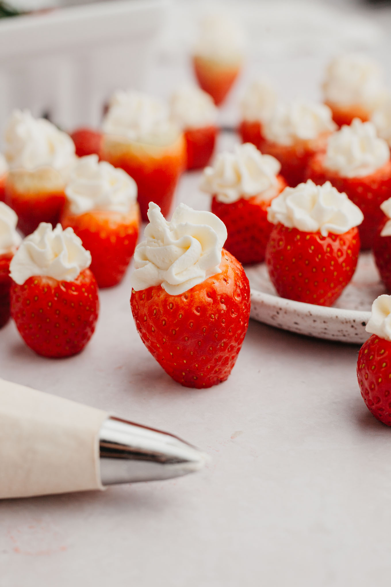 Stuffed strawberry cheesecake bites standing upright, with a piping bag in the foreground. 