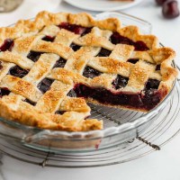 A cherry pie sitting on a wire rack with a slice taken out of it.