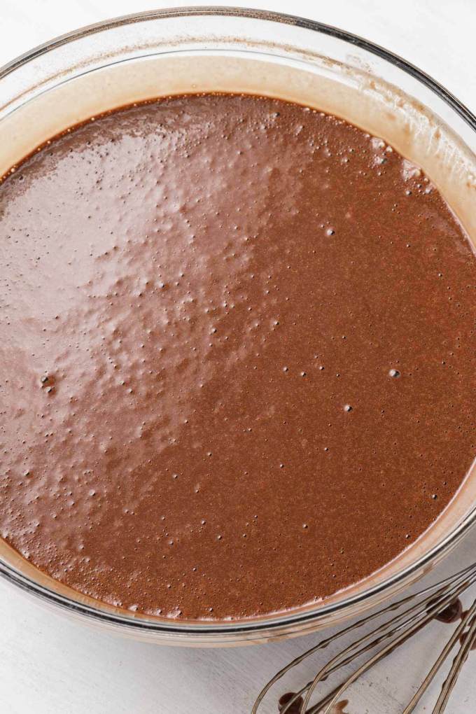 An overhead view of chocolate cake batter in a glass mixing bowl.