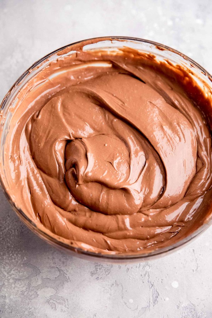 An overhead view of a smooth chocolate cheesecake filling in a glass mixing bowl.