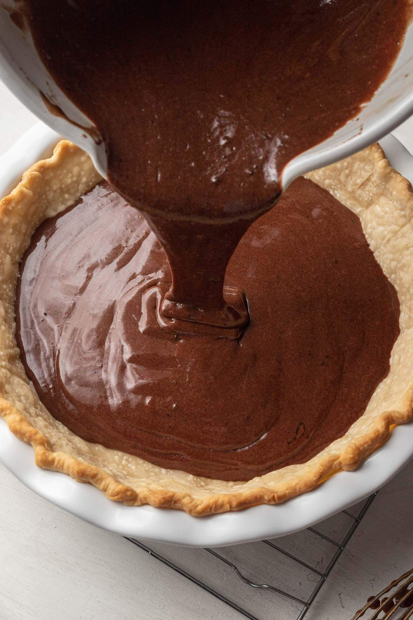 Chocolate chess pie filling being poured into a blind baked pie crust. 