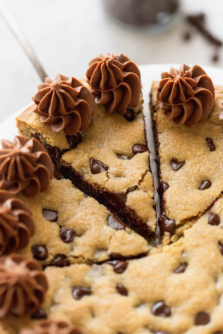 A chocolate chip cookie cake cut into slices and one being removed with a cake server.