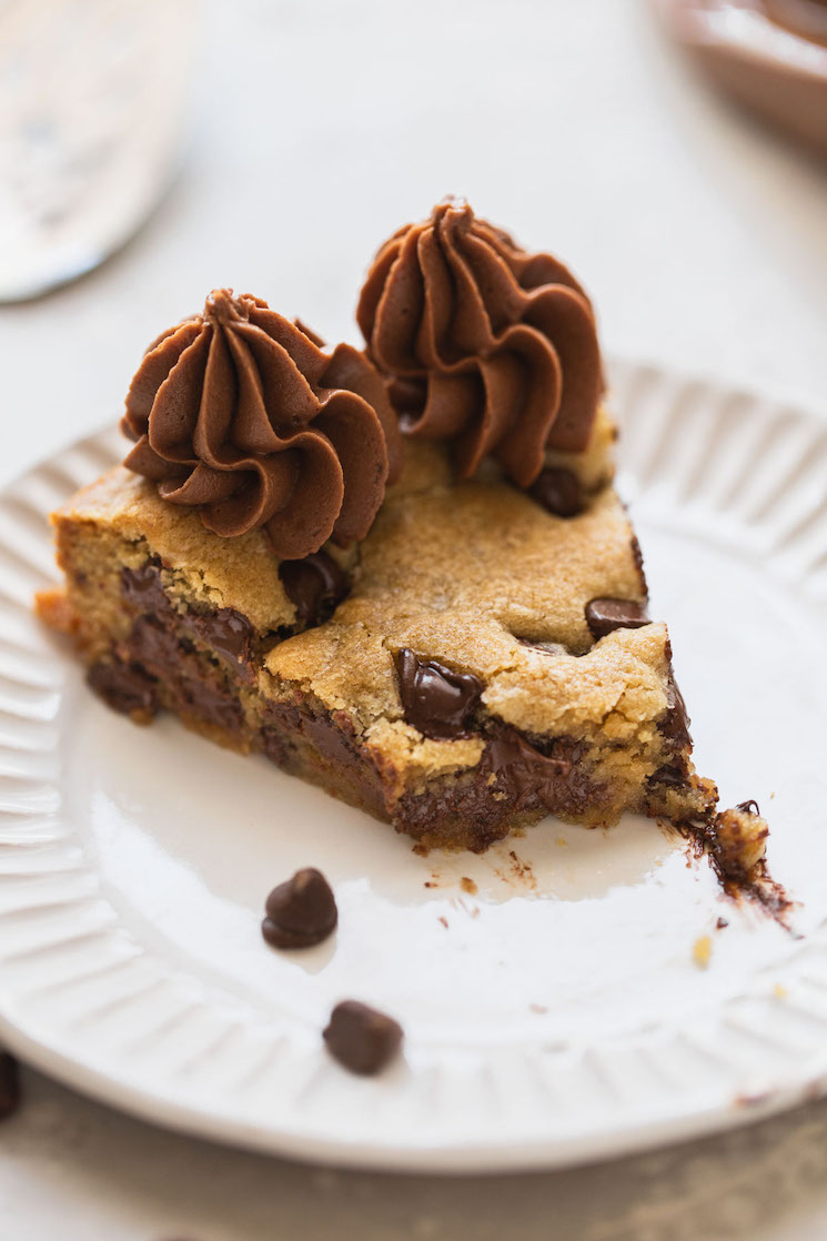 A single piece of cookie cake with a bite taken out of it on a white plate.