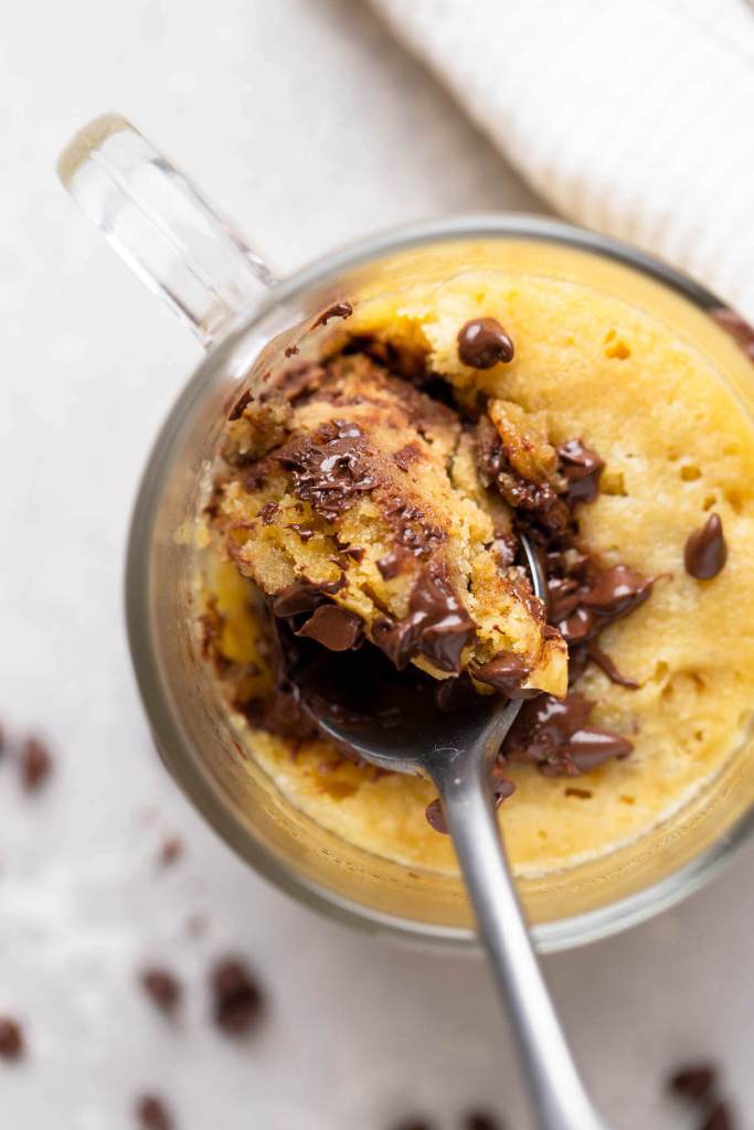 An overhead view of a spoon digging into the top of a microwave mug cookie. 