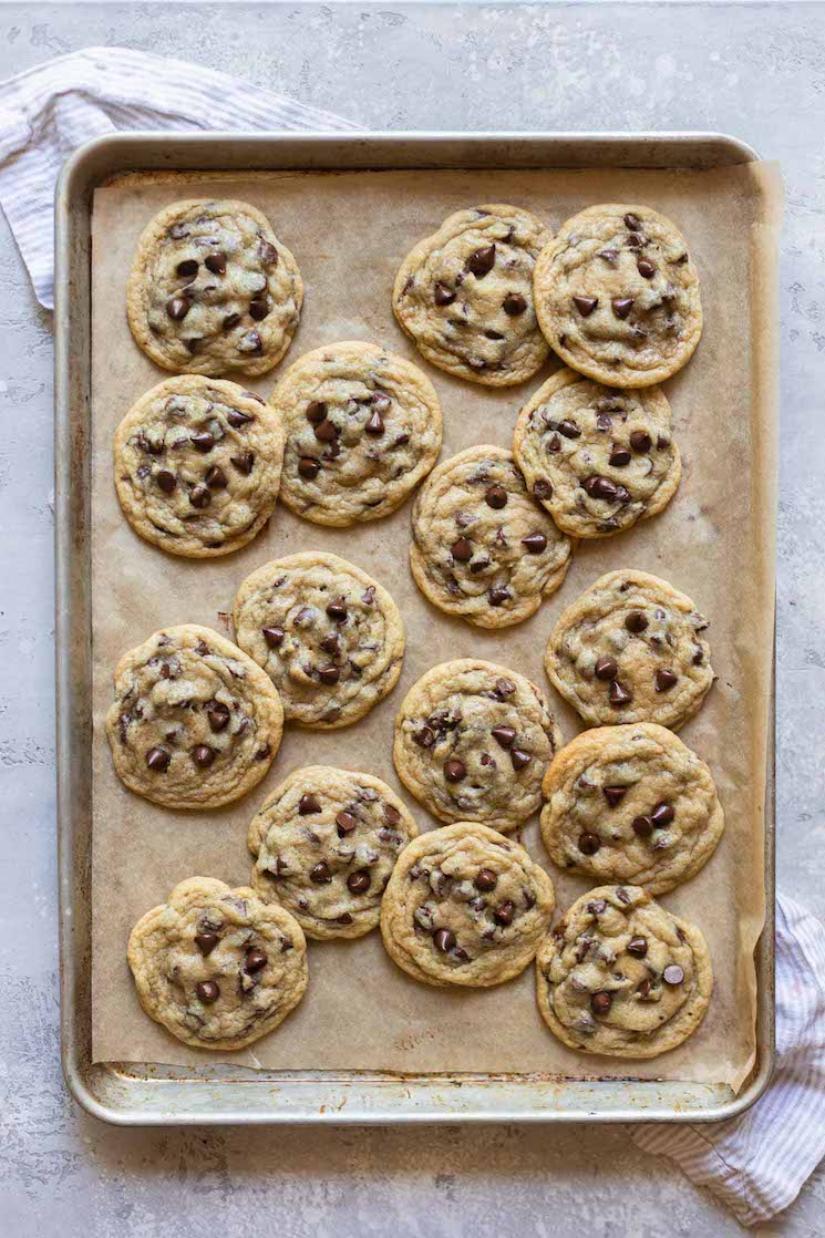 A baking sheet lined with brown parchment paper holding baked chocolate chip cookies.