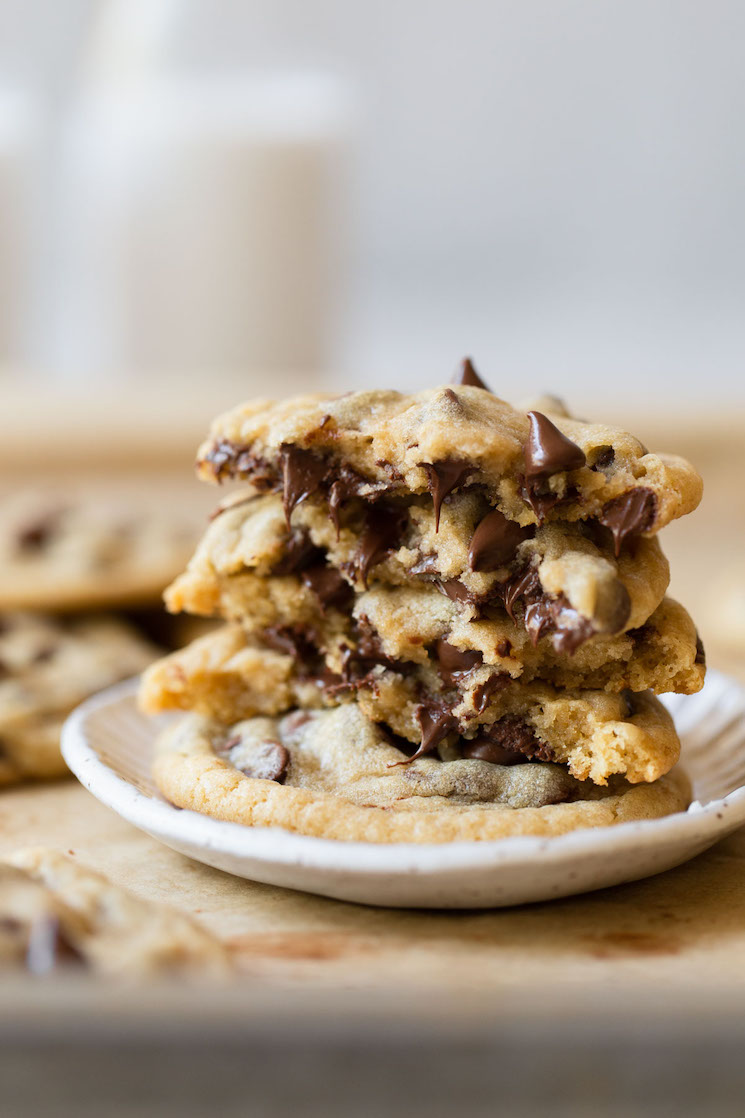 A stack of chocolate chip cookies on a white clay plate with more cookies in the background.