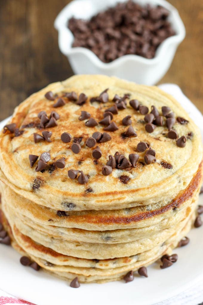 A stack of chocolate chip Greek yogurt pancakes. A dish of chocolate chips rests in the background. 