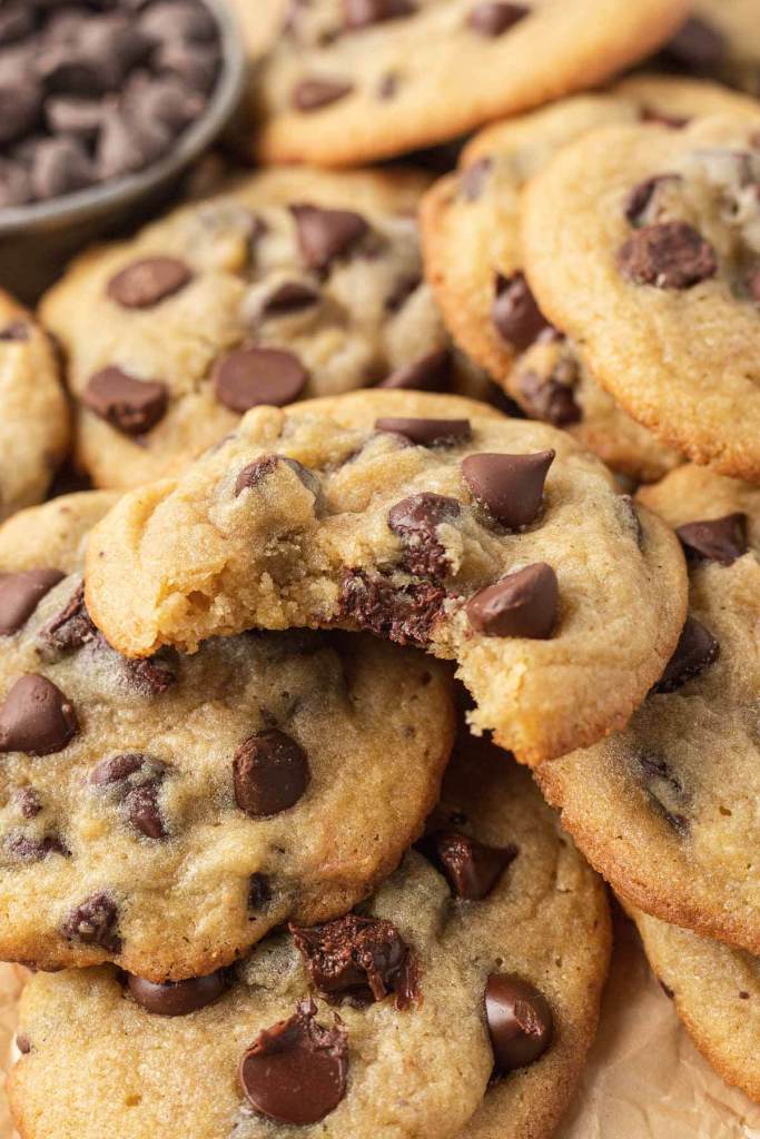 A close up view of a chocolate chip pudding cookie with a bite missing, on top of a pile of cookies. 