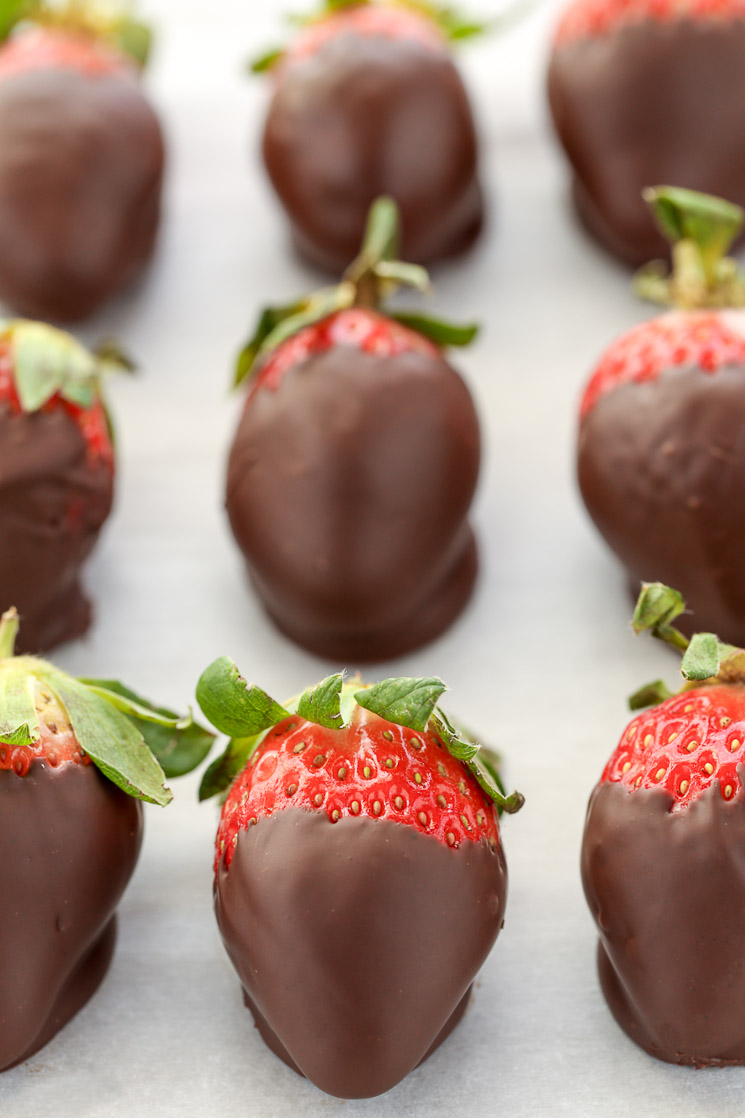 Chocolate covered strawberries lined up on a piece of parchment paper.