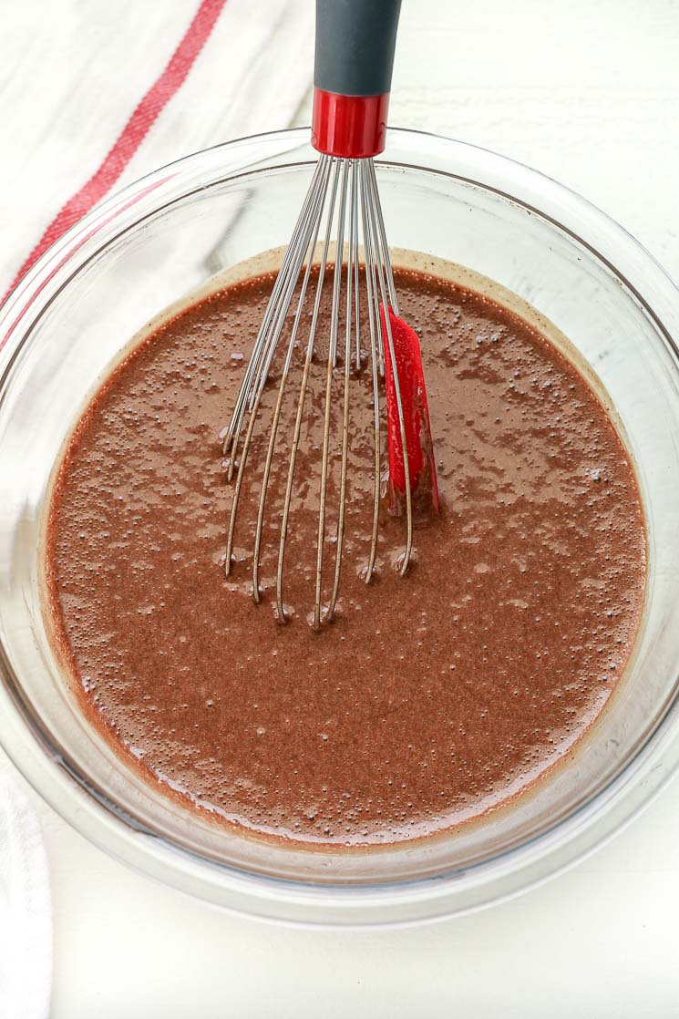 A clear bowl filled with chocolate cupcake batter and a whisk.