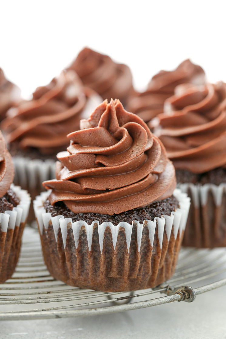 A close up picture of chocolate cupcakes topped with chocolate cream cheese frosting sitting on top of an antique round cooling rack. 