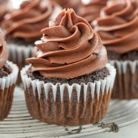 A close up picture of a chocolate cupcake topped with chocolate cream cheese frosting on an antique wire rack.