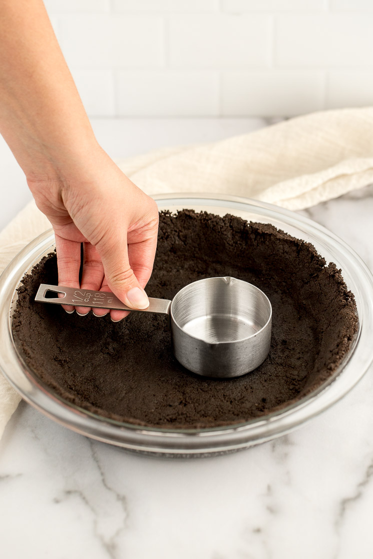 A homemade Oreo crust being pressed into a glass pie dish.