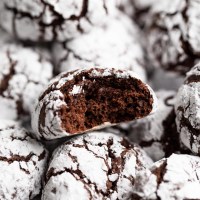 A batch of chocolate crinkle cookies with one cookie having a bite taken out of it.