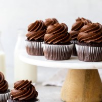 Several chocolate cupcakes on top of a marble cake stand.