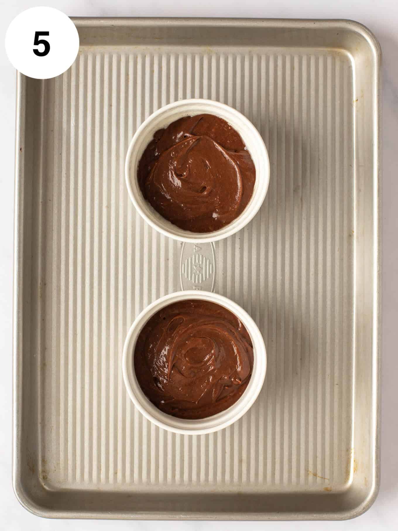 An overhead view of chocolate lava cake batter in two ramekins on a baking sheet.