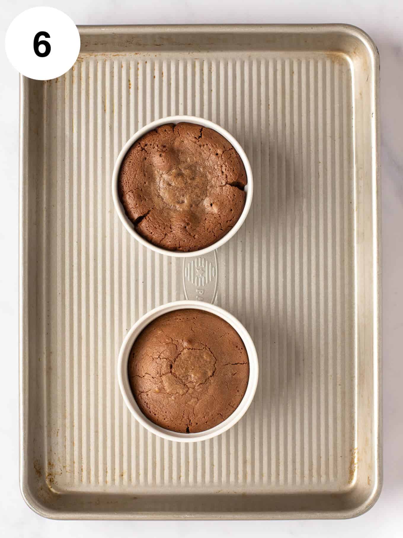 An overhead view of two baked chocolate lava cakes on a baking sheet.