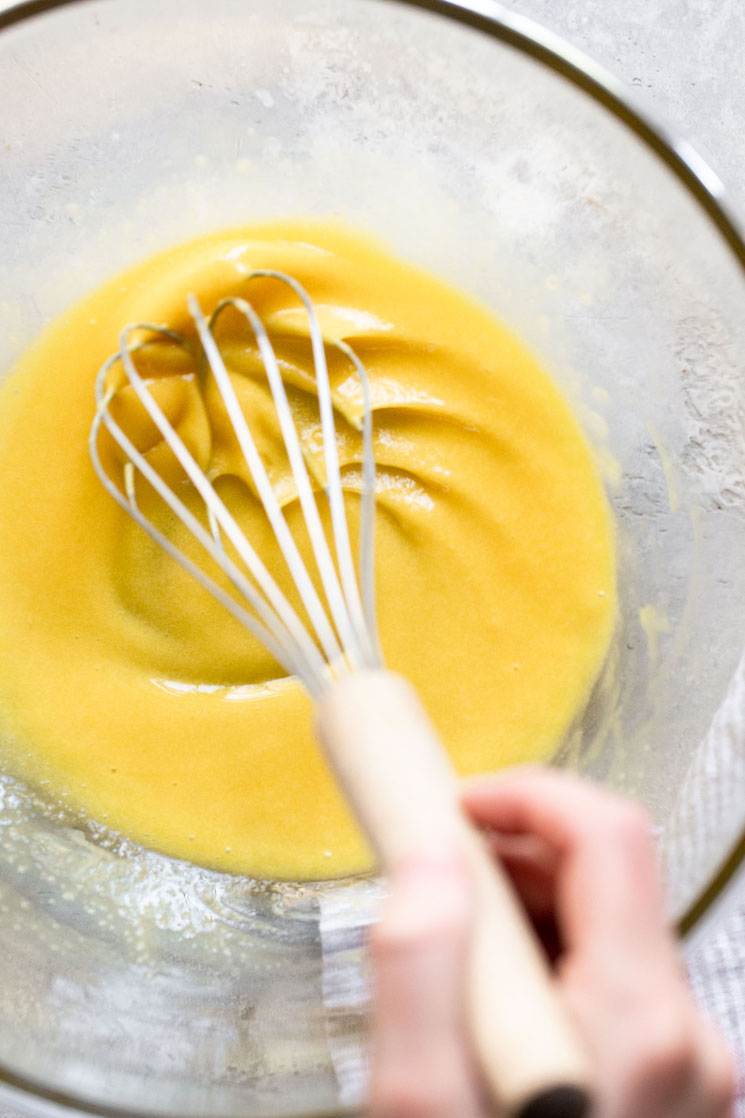 A glass bowl with eggs and sugar being mixed together with a whisk.