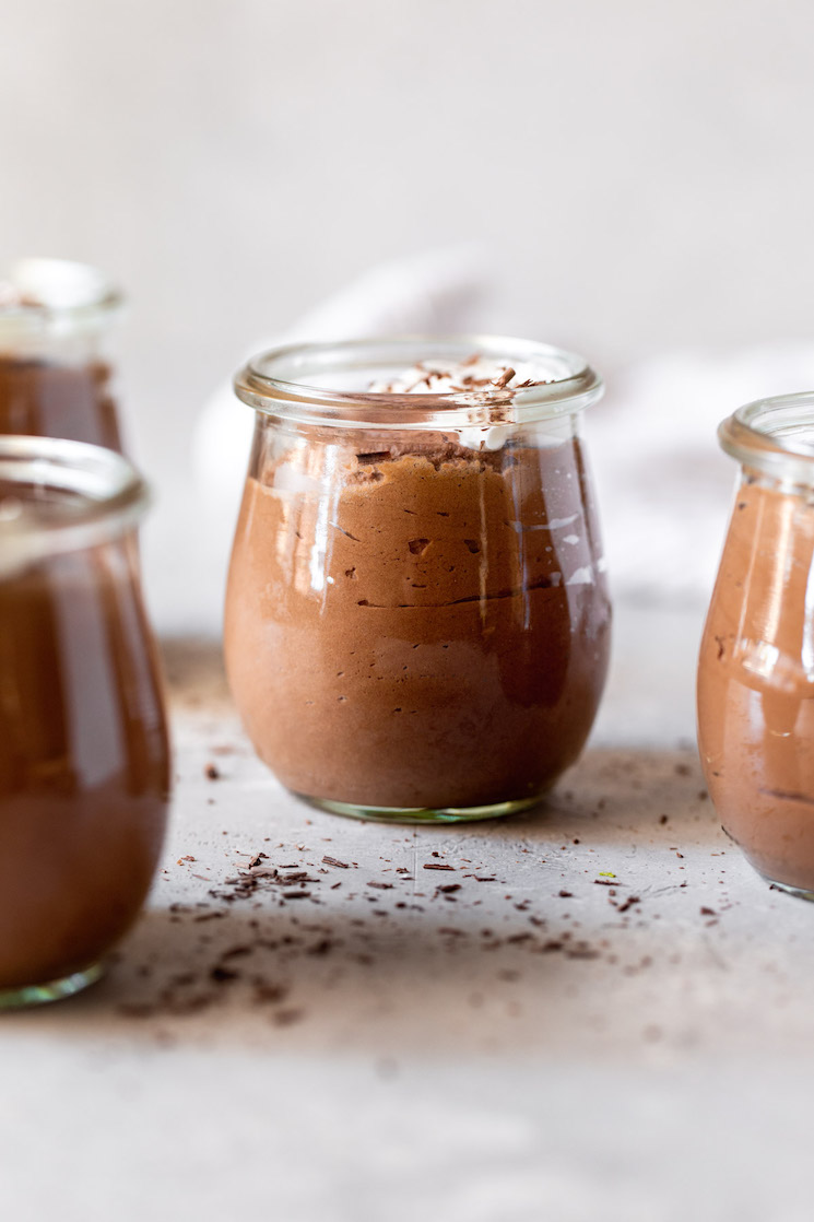 Multiple small glass jars filled with chocolate mousse topped with whipped cream and chocolate shavings.