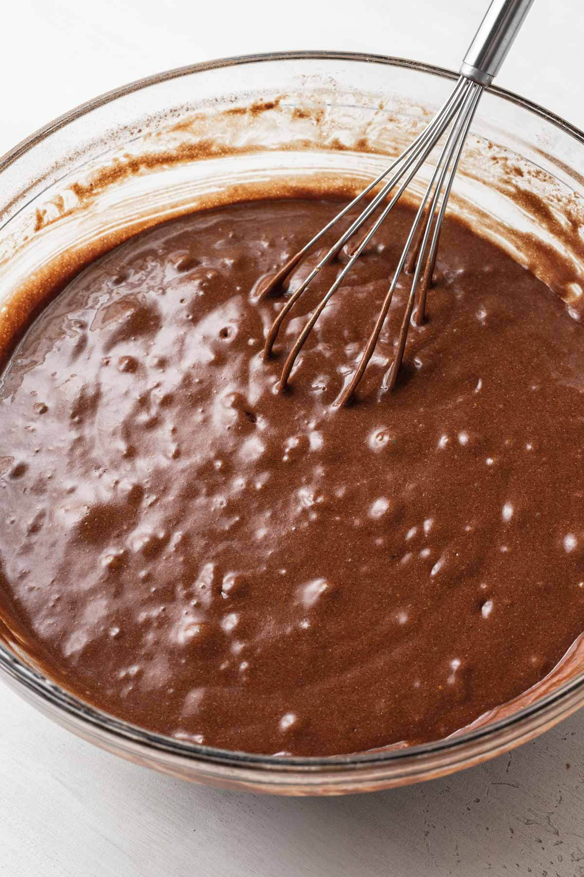 Chocolate cake batter in a glass mixing bowl with a whisk.