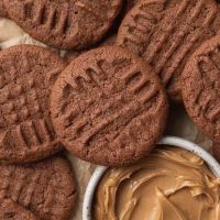 An overhead view of several chocolate peanut butter cookies. One of the cookies is resting against a small bowl of peanut butter.