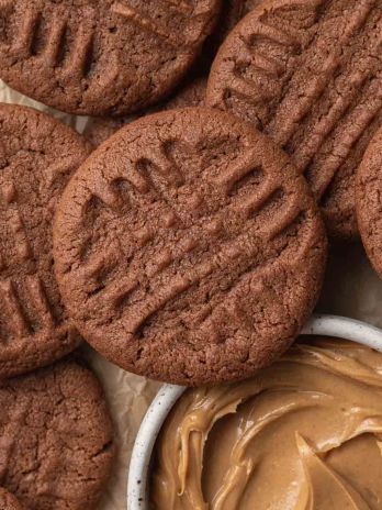 An overhead view of several chocolate peanut butter cookies. One of the cookies is resting against a small bowl of peanut butter.