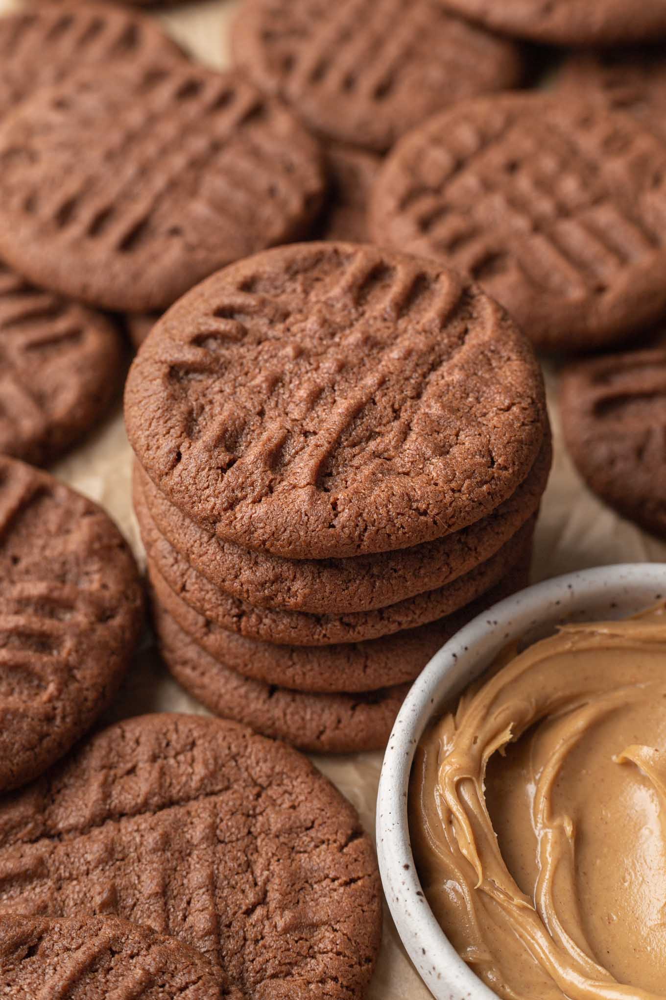 A stack of chocolate peanut butter cookies next to a dish of peanut butter. 