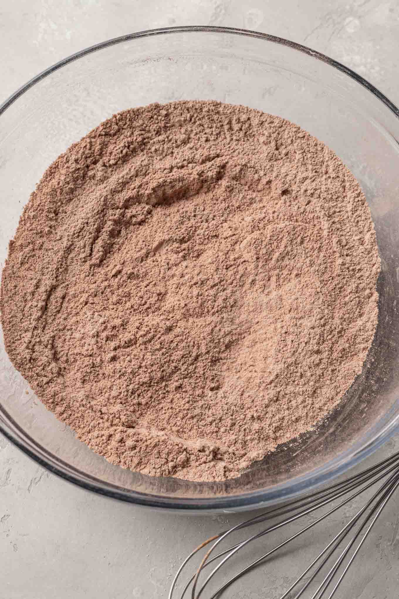 An overhead view of flour and cocoa powder in a glass mixing bowl. 