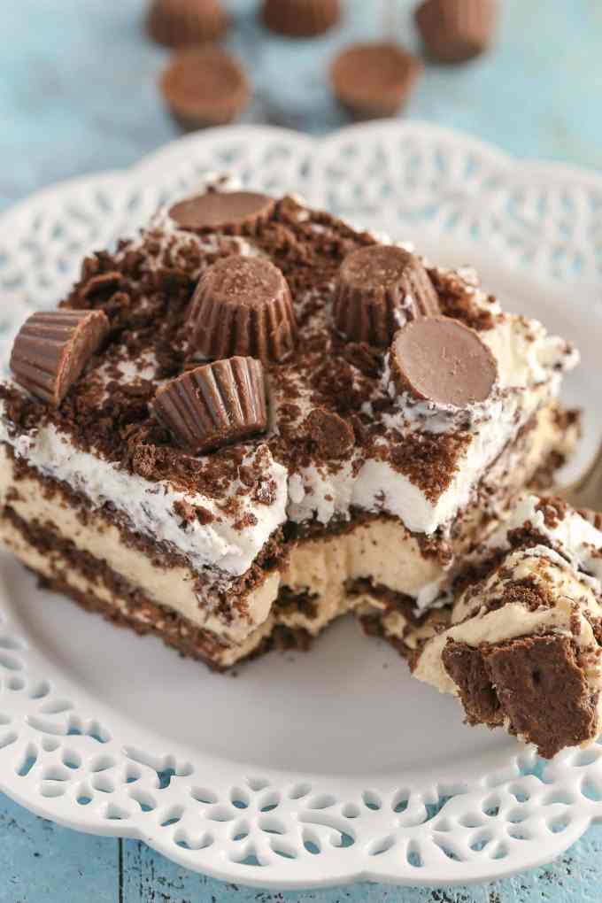 A slice of peanut butter chocolate icebox cake on a white plate with a fork. Mini PB cups rest in the background. 