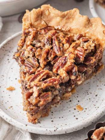 A slice of chocolate pecan pie on a speckled white plate.