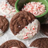 A chocolate cookie coated in white chocolate and crushed candy canes leaning up against a small dish.