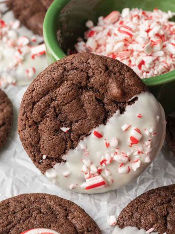 A chocolate cookie coated in white chocolate and crushed candy canes leaning up against a small dish.