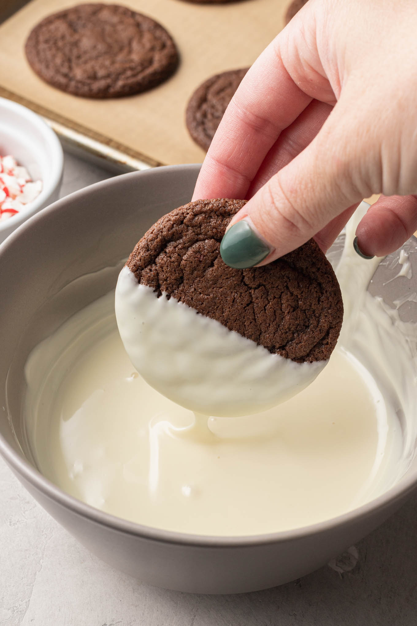 A process shot chowing a chocolate peppermint cookie being dipped in white chocolate. 