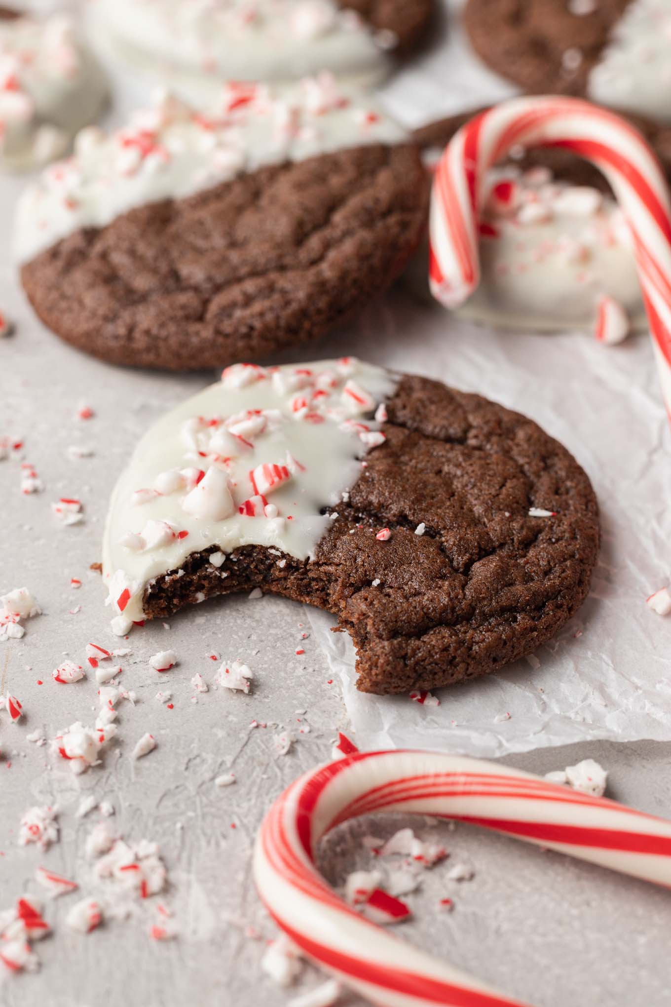 A chocolate peppermint Christmas cookie with a bite missing, surrounded by additional cookies. 