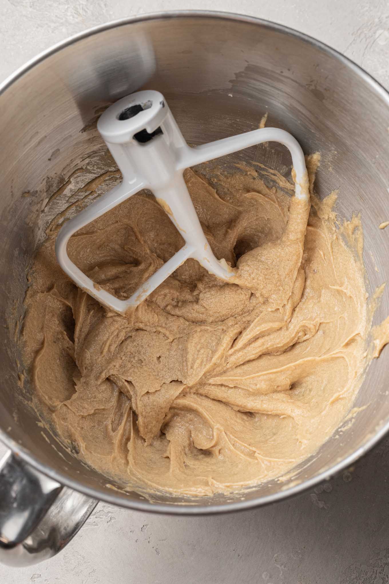 An overhead view of creamed butter and sugar in the bowl of a stand mixer, with a paddle attachment. 