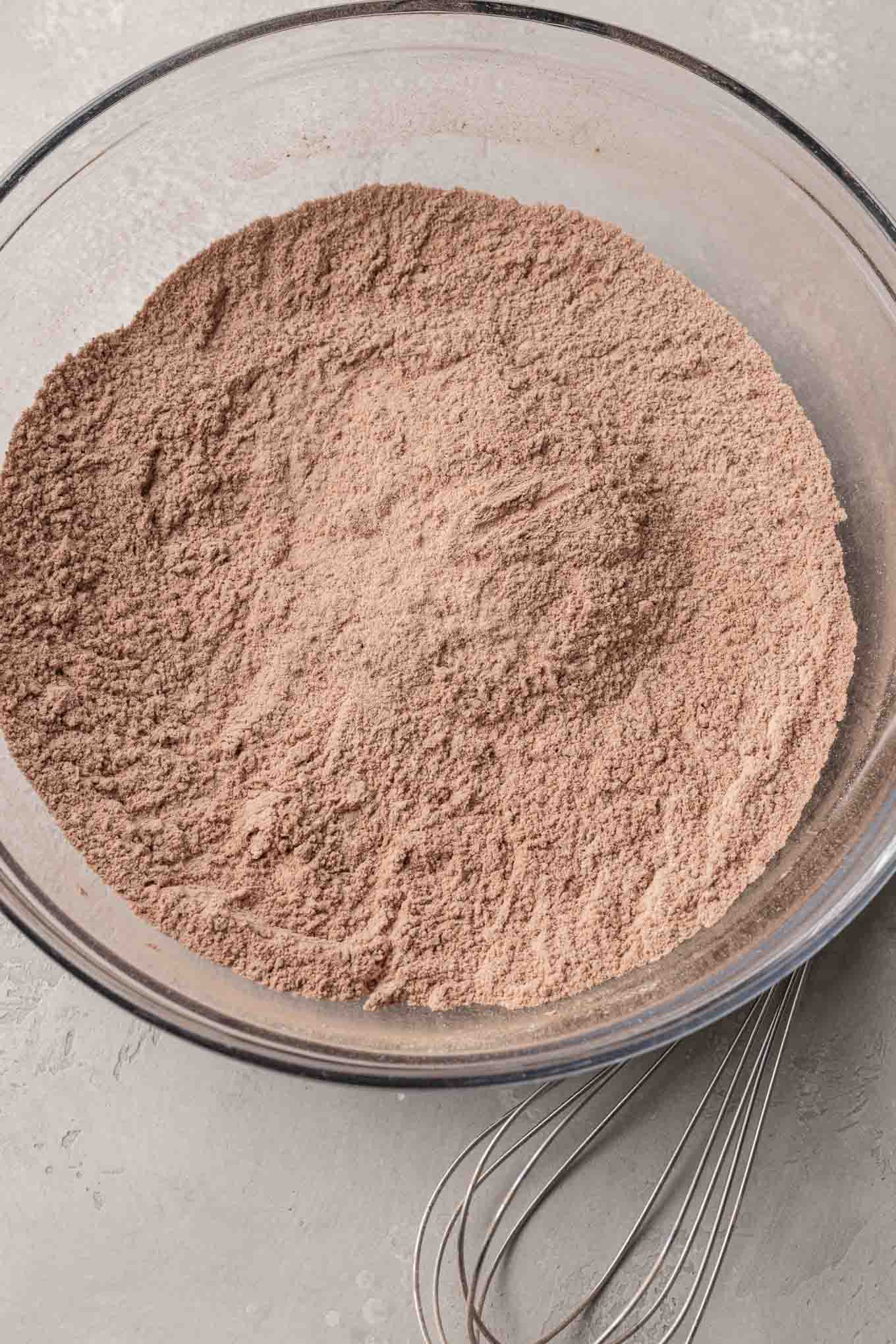 An overhead view of flour, cocoa powder, baking soda, and salt in a glass mixing bowl. 