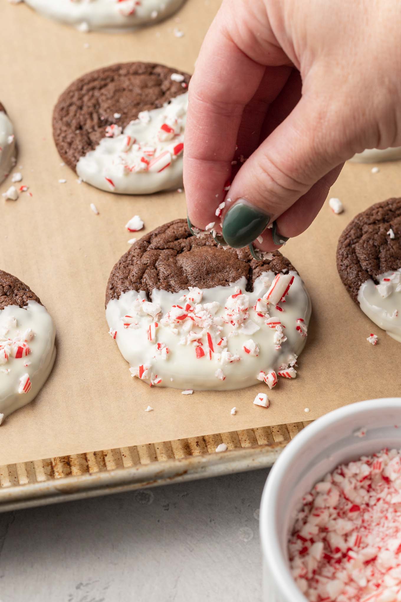 A process shot chowing a chocolate peppermint cookie being topped with crushed candy cane pieces. 