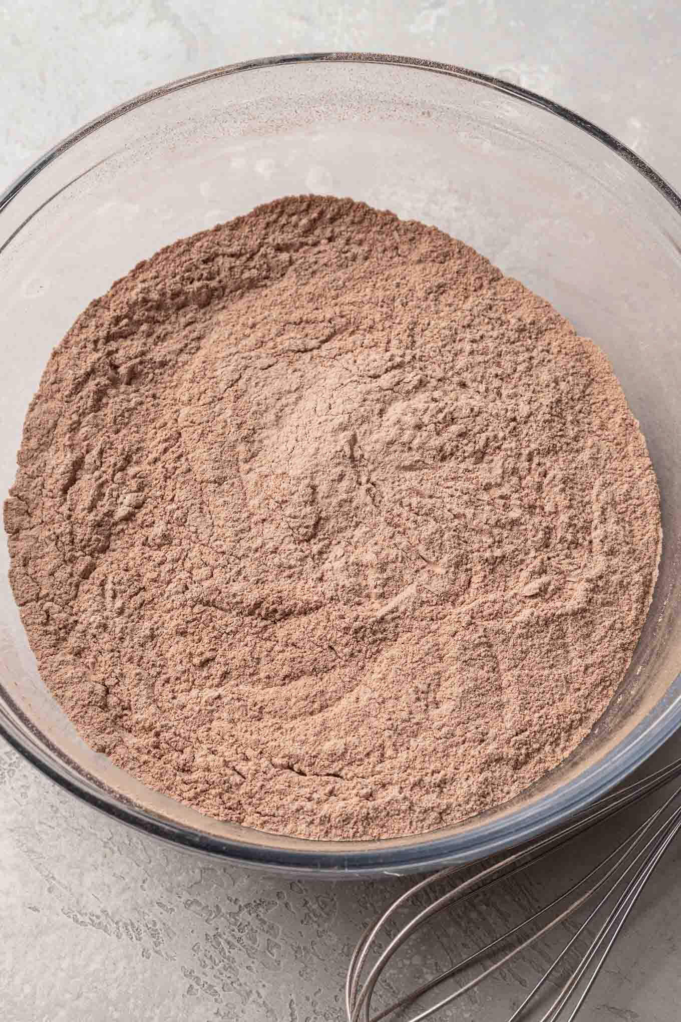 An overhead view of cocoa powder and flour sifted together in a glass mixing bowl. 