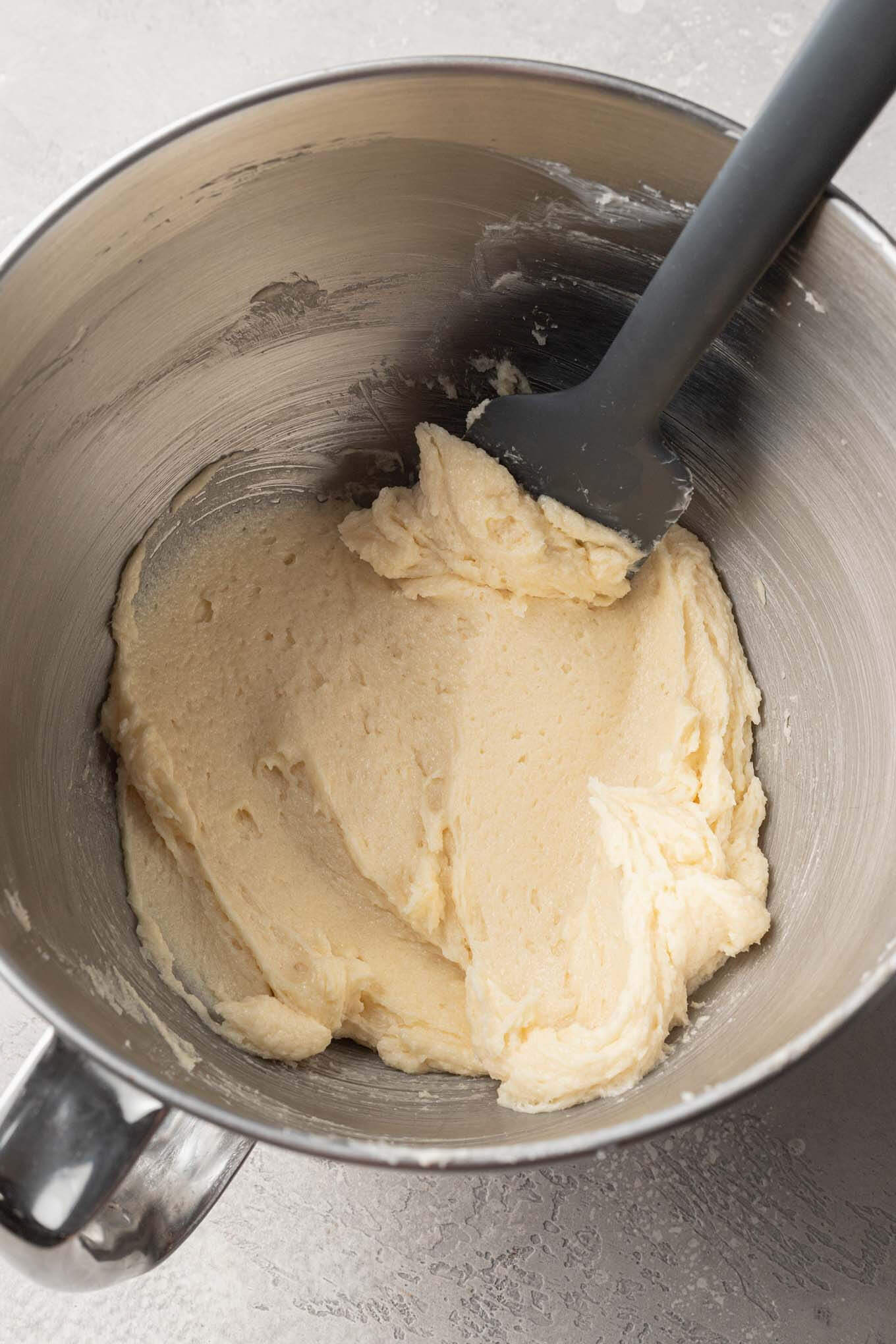 An overhead view of the wet ingredients needed for sugar cookies in a mixing bowl, with a rubber spatula.  