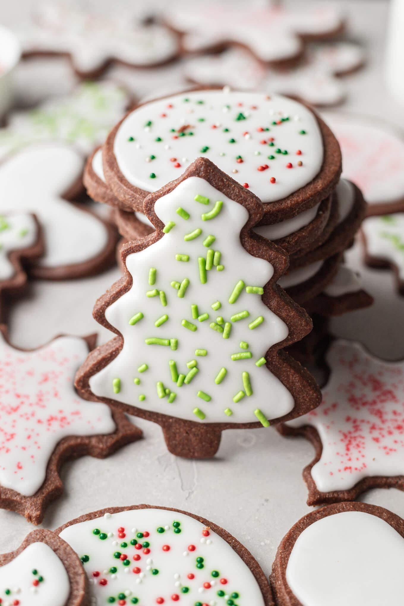 A stack of chocolate sugar cookies, decorated with icing and sprinkles. A tree-shaped cookie leans against the stack. 