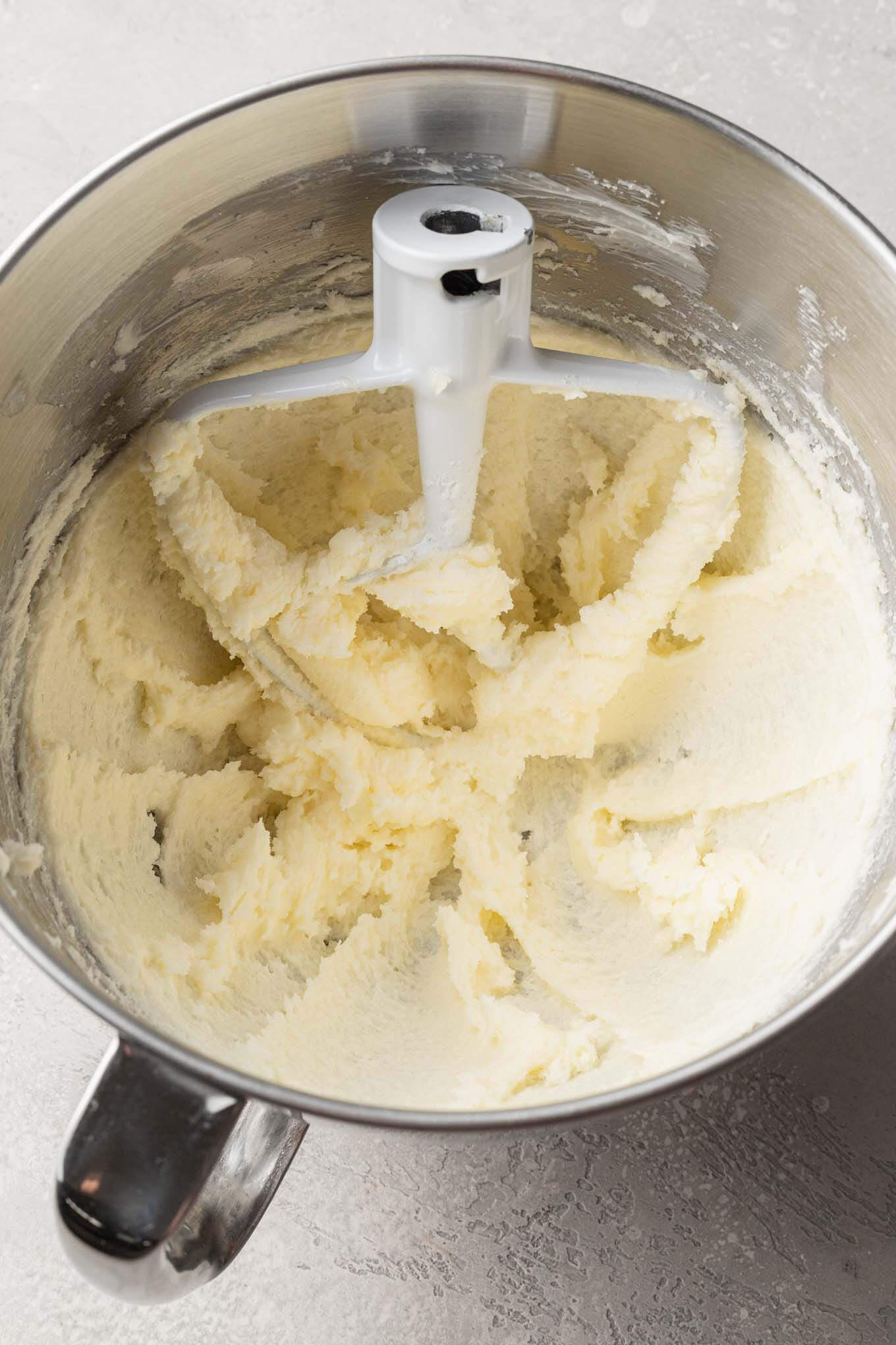 An overhead view of butter and sugar in a mixing bowl with a paddle attachment from a stand mixer. 