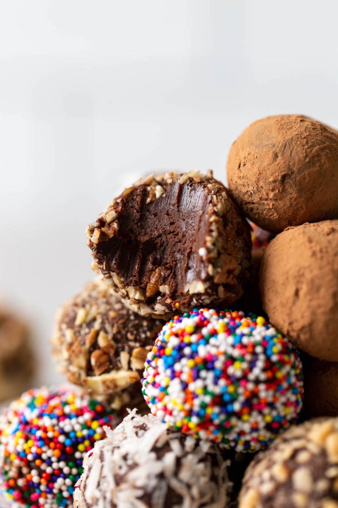 A close up view of homemade truffles in a pile. One truffle has a bite missing. 