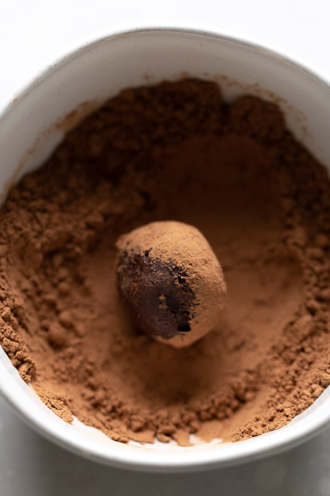 A homemade truffle being coated in cocoa powder.