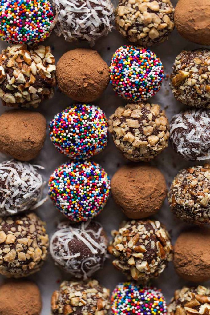 Overhead view of four rows of chocolate truffles covered in various coatings. 