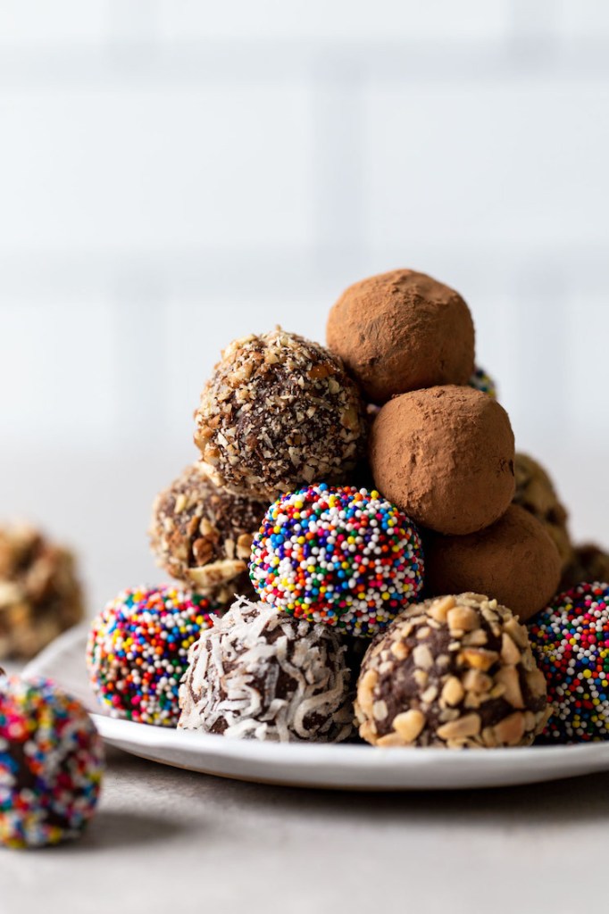 A pile of homemade chocolate truffles on a white dessert plate. The truffles are coated in various coatings. 