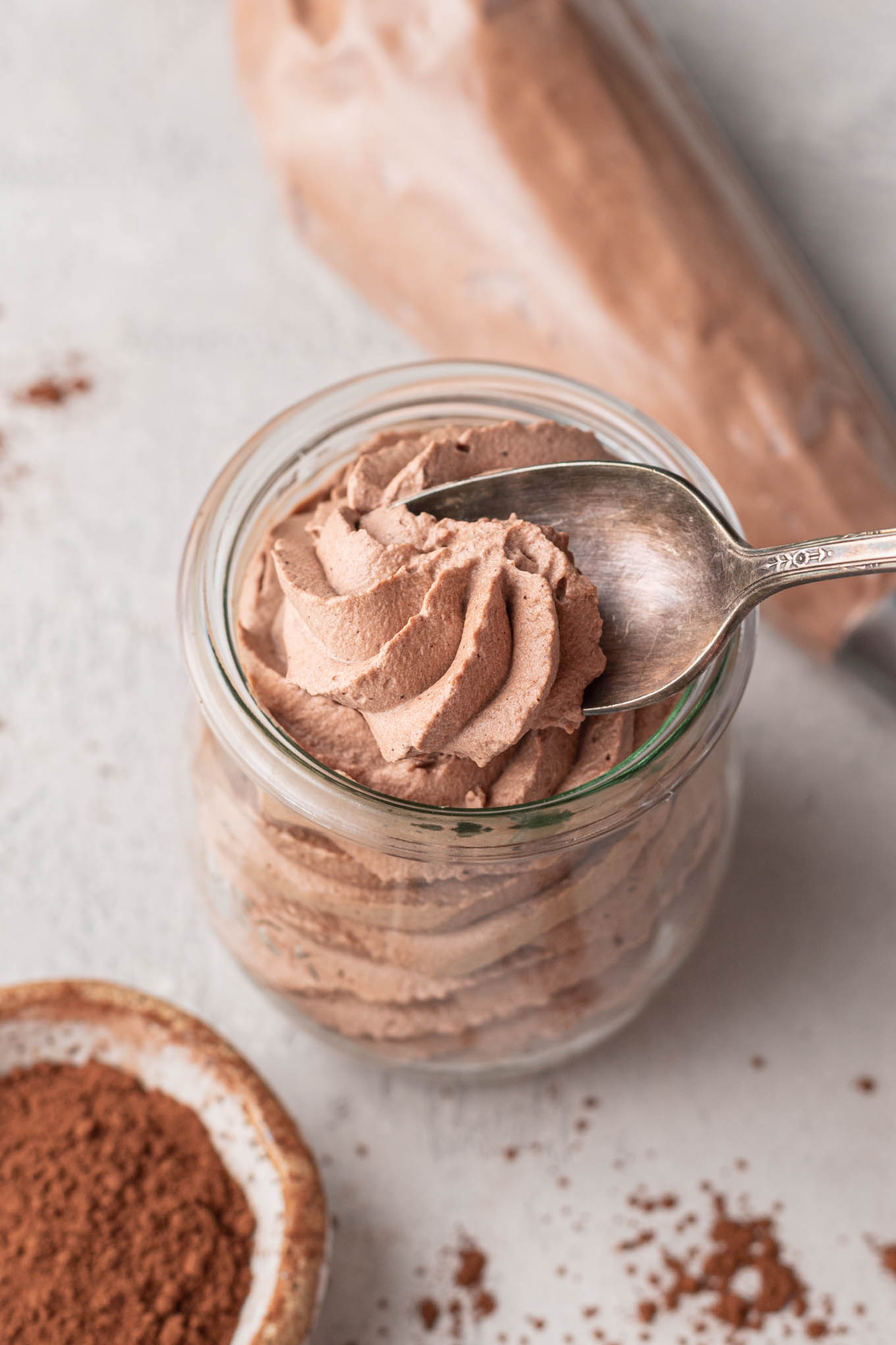 A small jar filled with chocolate whipped cream. A spoon is taking a small scoop out of the whipped cream.