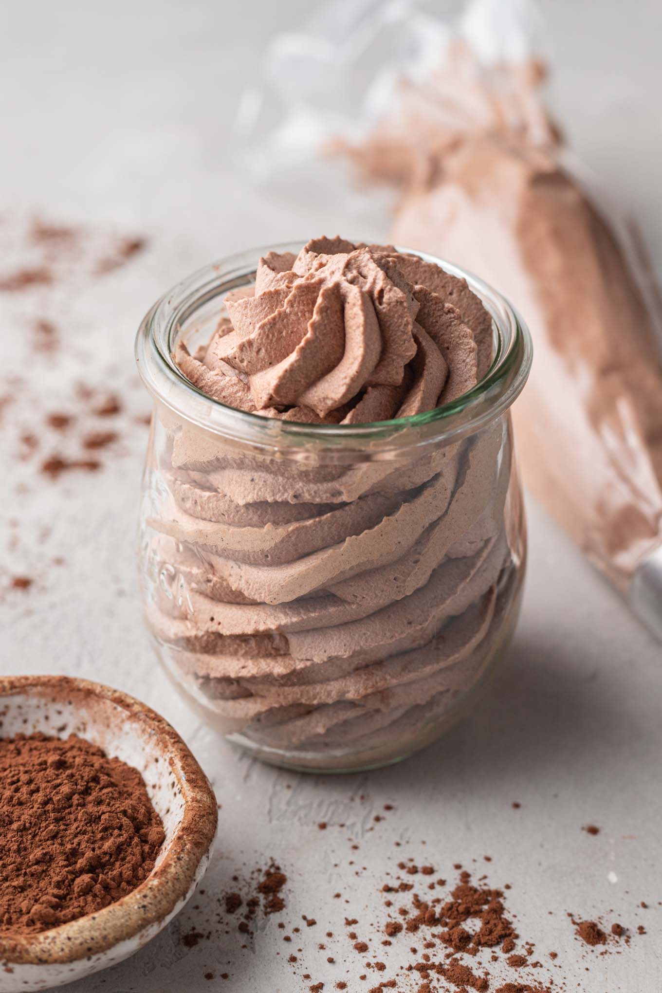 A jar of chocolate whipped cream with a small bowl of Dutch process cocoa powder resting next to it.